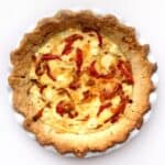 A Three-Cheese Quiche with Roasted Bell Peppers features a golden-brown crust, filled with cheese and sweet red bell peppers, all baked to perfection in a white ceramic pie dish.