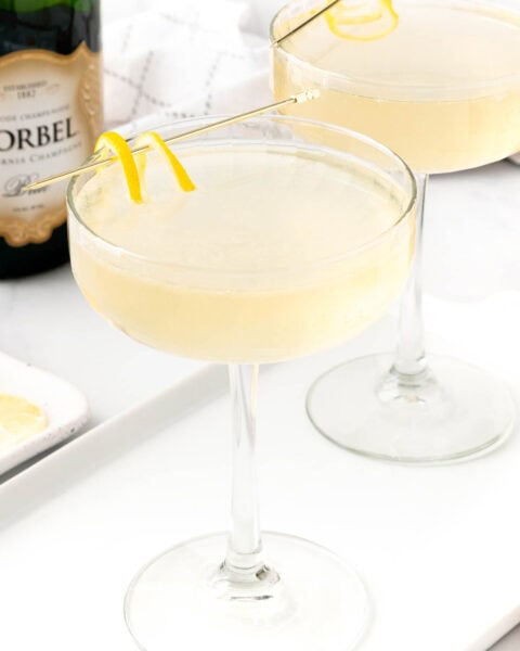 Two glasses of French 75 champagne on a tray with a bottle of champagne.