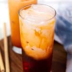 two glasses of spiked thai iced tea with milk on a wooden board