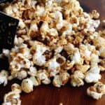 A box of Chipotle Lime Popcorn is spilled onto a wooden surface, with zesty popcorn kernels scattered around.