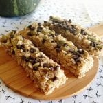Four Pumpkin Chocolate Chip Granola Bars topped with pumpkin seeds and chocolate chips are arranged on a round wooden board.