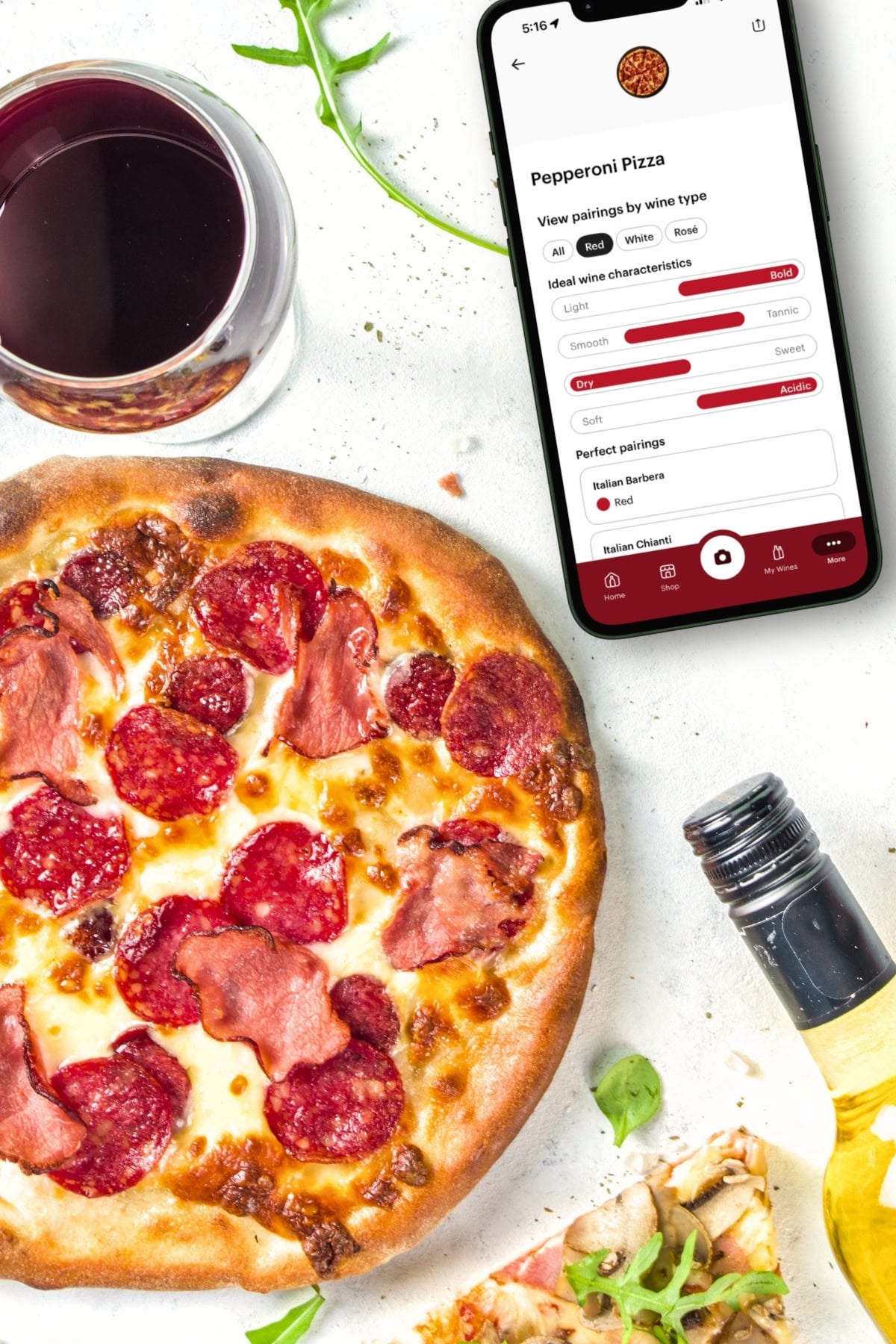 A pepperoni pizza, a glass of red wine, a smartphone displaying the best Cooking Apps for pizza and wine pairing, and a bottle of white wine on a white surface with scattered arugula.