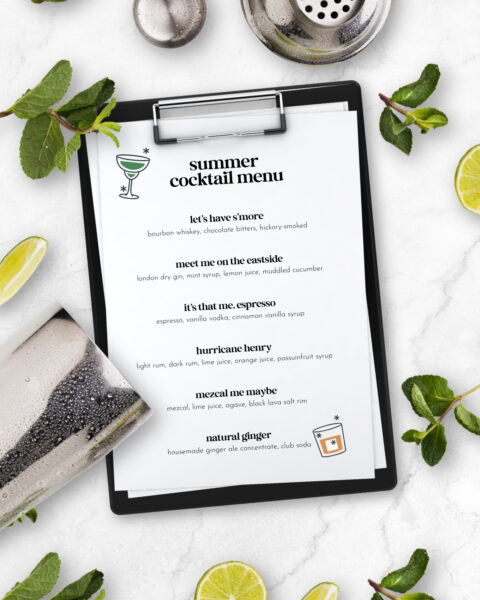 Clipboard with a summer cocktail menu, surrounded by mint, lime slices, a drink, and a cocktail strainer—perfect inspiration for crafting a home cocktail menu.