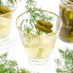 A glass of pickled martini juice garnished with dill and pickles, with a jar of pickles nearby.