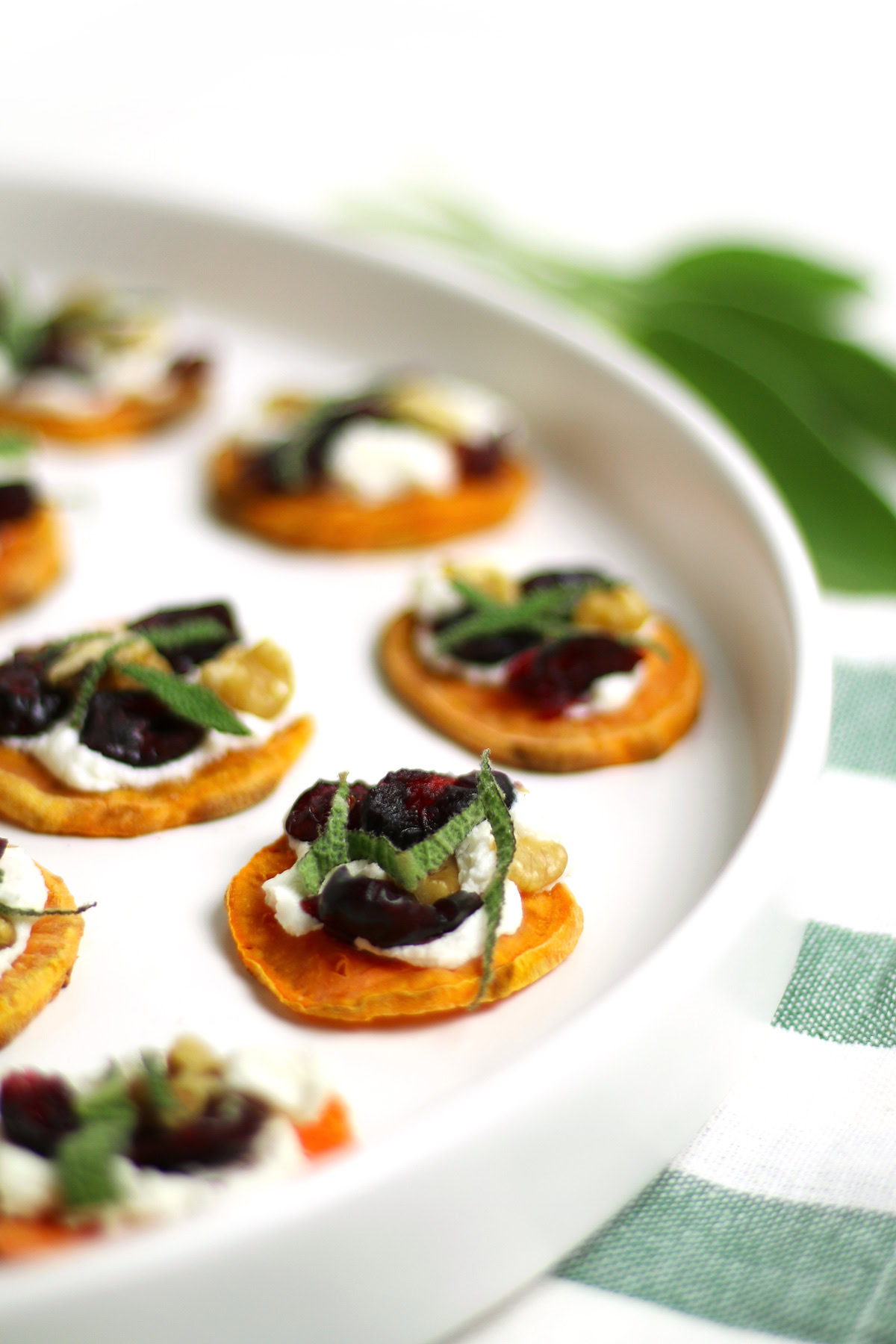 Holiday Sweet Potato Toast Bites: Sweet potato rounds topped with cheese, herbs, and dried fruit arranged on a white plate.