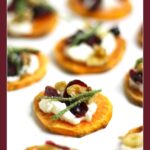 Holiday Sweet Potato Toast Bites: Crispy sweet potato rounds topped with cheese, nuts, cranberries, and herbs on a white plate.