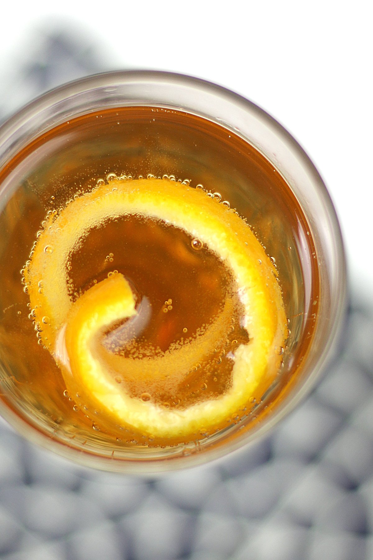 A close-up view of a Seelbach Bourbon Champagne Cocktail with a lemon twist garnish, seen from above, on a patterned surface.