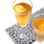 A Seelbach Bourbon Champagne Cocktail fills a champagne flute with a golden-brown drink, garnished with a lemon twist and set on a patterned napkin.