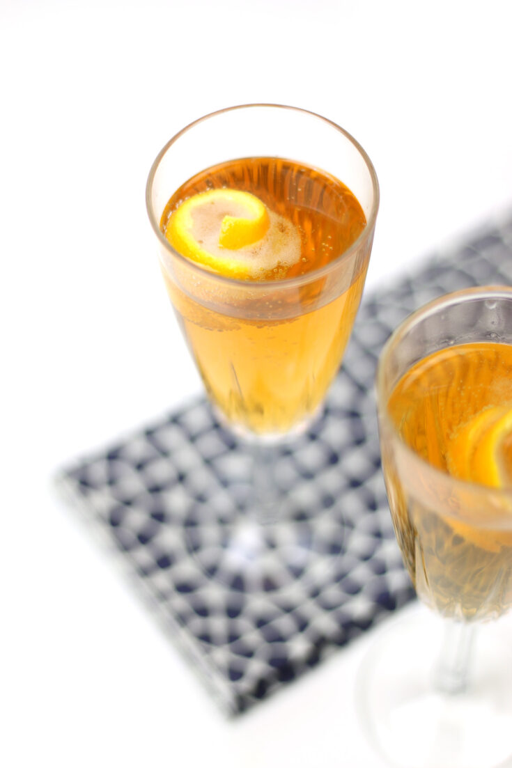 A Seelbach Bourbon Champagne Cocktail fills a champagne flute with a golden-brown drink, garnished with a lemon twist and set on a patterned napkin.