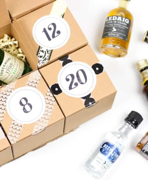A charming alcohol Advent Calendar featuring a set of small liquor bottles nestled beside a gift box with numbered compartments, some of which are delightfully open.