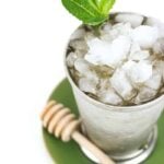 a honey whiskey mint julep garnished with a mint sprig in a silver julep cup on a green plate with a honey wand