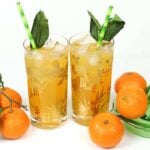 Two glasses of Mandarin Orange Gin & Tonic with ice and green leaves.