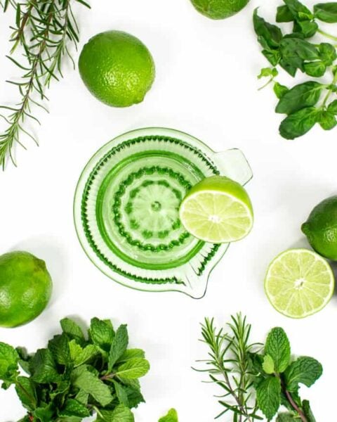 prep shot of green glass citrus juicer with fruits and herbs