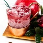 a pomegranate yule mule with a leafy garnish and pomegranate seeds on top