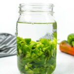 a jar of hatch chiles infusing with vodka on a textured white background