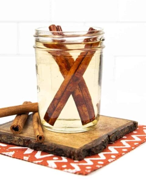 a jar of cinnamon simple syrup next to cinnamon sticks on a wooden coaster