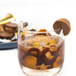 a peanut butter old-fashioned on a white background with a blue plate of peanut butter cup candies in the background