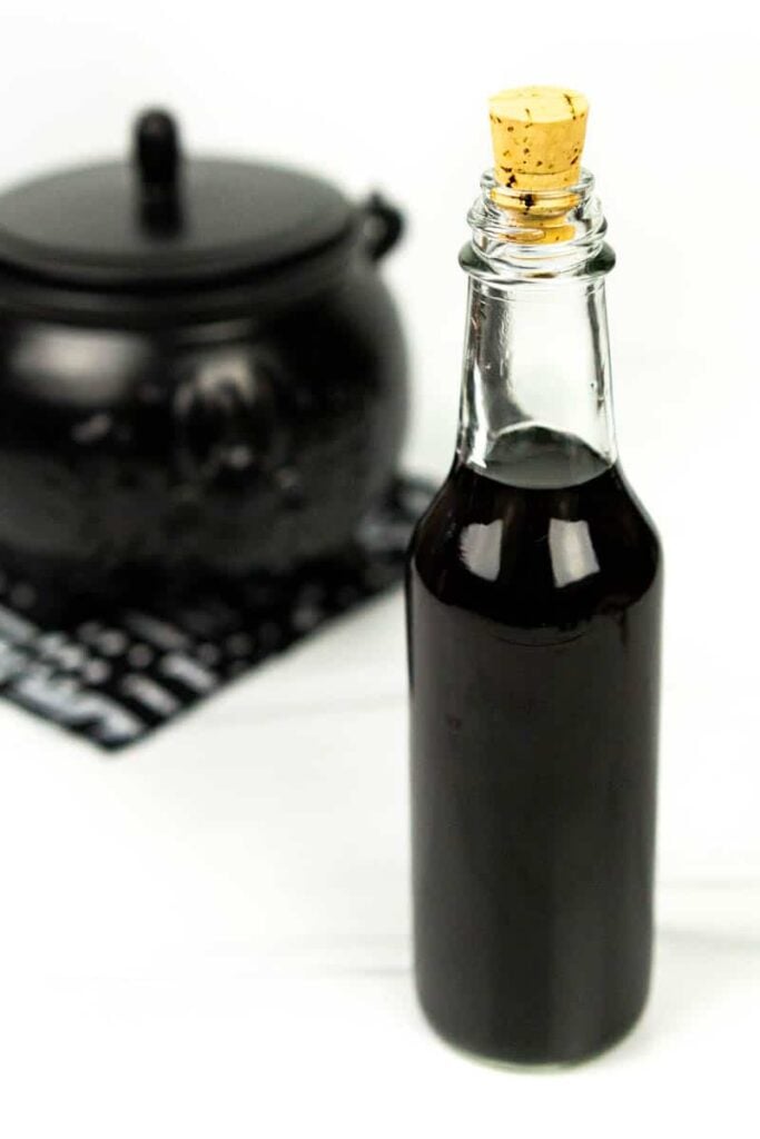 a bottle of black vodka with a cork next to a Halloween cauldron on a black and white napkin