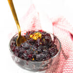 a glass dish of orange bourbon cranberry sauce next to a red and white kitchen towel