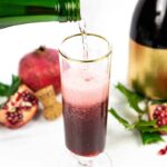 a green champagne bottle pours champagne into a pomegranate mimosa
