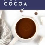 Overhead view of a mug filled with instant pot hot chocolate, surrounded by chocolate chips, marshmallows, and a striped towel. Text reads "easy homemade hot cocoa, get the recipe.