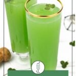 Two tall glasses filled with vibrant green mimosas, each garnished with a small clover leaf, sit on a white surface with corks and clover leaves nearby.