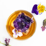 a cocktail with a pansy ice cube and a violet garnish