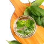 a jar of basil syrup on a wood board with fresh basil