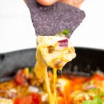 Cheesy chorizo dip is lifted up by a tortilla chip as the cheese stretches.