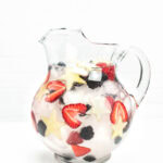 ice, berries and apples floating in a pitcher of water