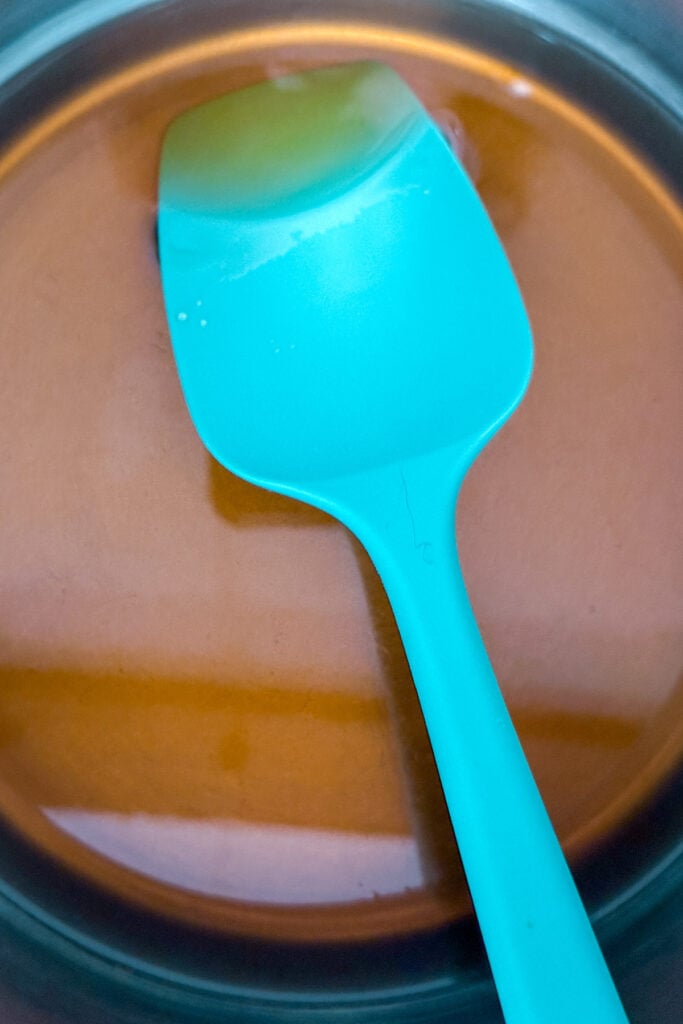 A turquoise spatula rests in a glass bowl containing brown demerara syrup.