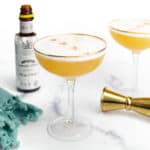 two whiskey sours with a bottle of bitters