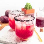 pink margaritas garnished with black salt on the rim