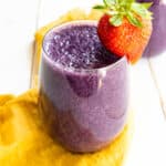 a strawberry on the rim of the glass of a berry smoothie