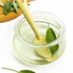 a sage leaf and a yellow spoon in a jar of sage syrup