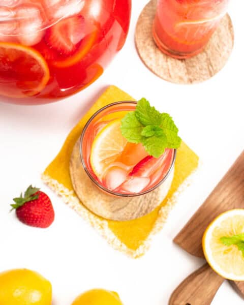 a pitcher of strawberry lemonade with a couple of glasses and lemons