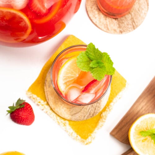a pitcher of strawberry lemonade with a couple of glasses and lemons
