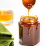 a spoon dripping caramel sauce into a jar
