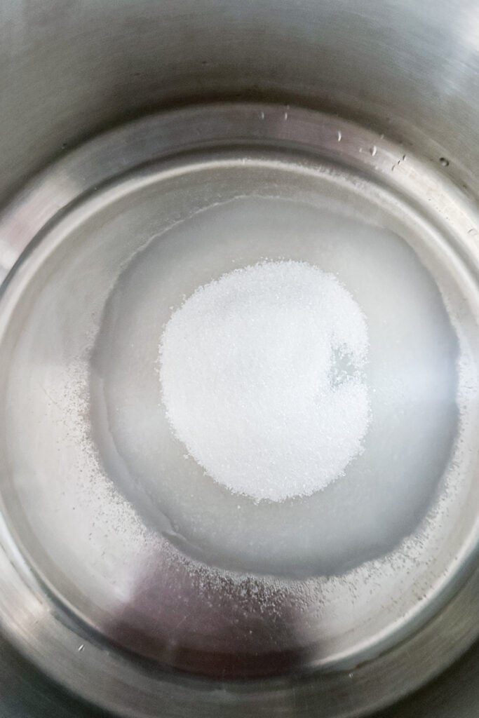 Old-fashioned simple syrup begins with granulated white sugar partially dissolved in water at the bottom of a stainless steel pot.