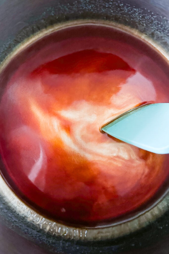 A close-up of a light blue spatula stirring a pot of red sauce with visible swirls, viewed from above—perfect for prepping an old-fashioned simple syrup or any homemade creation.