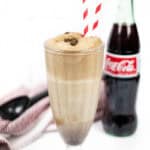 A boozy ice cream float sits next in front of a glass bottle of Coca-Cola and a black ice cream scoop.