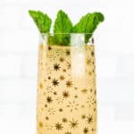 A glass with gold star pattern holds a bubbly mimosa garnished with green herb leaves