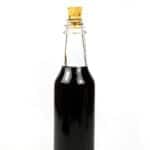 glass bottle of homemade black vodka with cork on white background