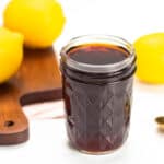 jar of infused sweet tea vodka with brown wooden cutting board, gold spoon and lemons in background