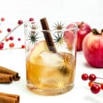 A seasonal fall old-fashioned is flanked by cinnamon sticks and red apples