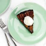 A chocolate pie with nuts on top and a scoop of ice cream on a light green plate with two forks