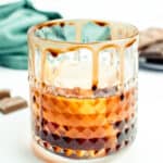 Closeup of a chocolate old-fashioned cocktail in a rocks glass with chocolate rim and chocolate out of focus in the background