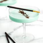 Two grasshopper drinks on a marble countertop and garnished with chocolate shavings and chocolate cookie sticks.
