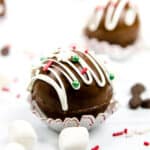 A hot chocolate bomb with marshmallows and chocolate chips and sprinkles on a marble background.