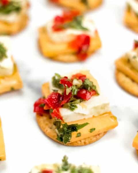 A close up shot of marinated cheese on a cracker with other crackers out of focus surrounding